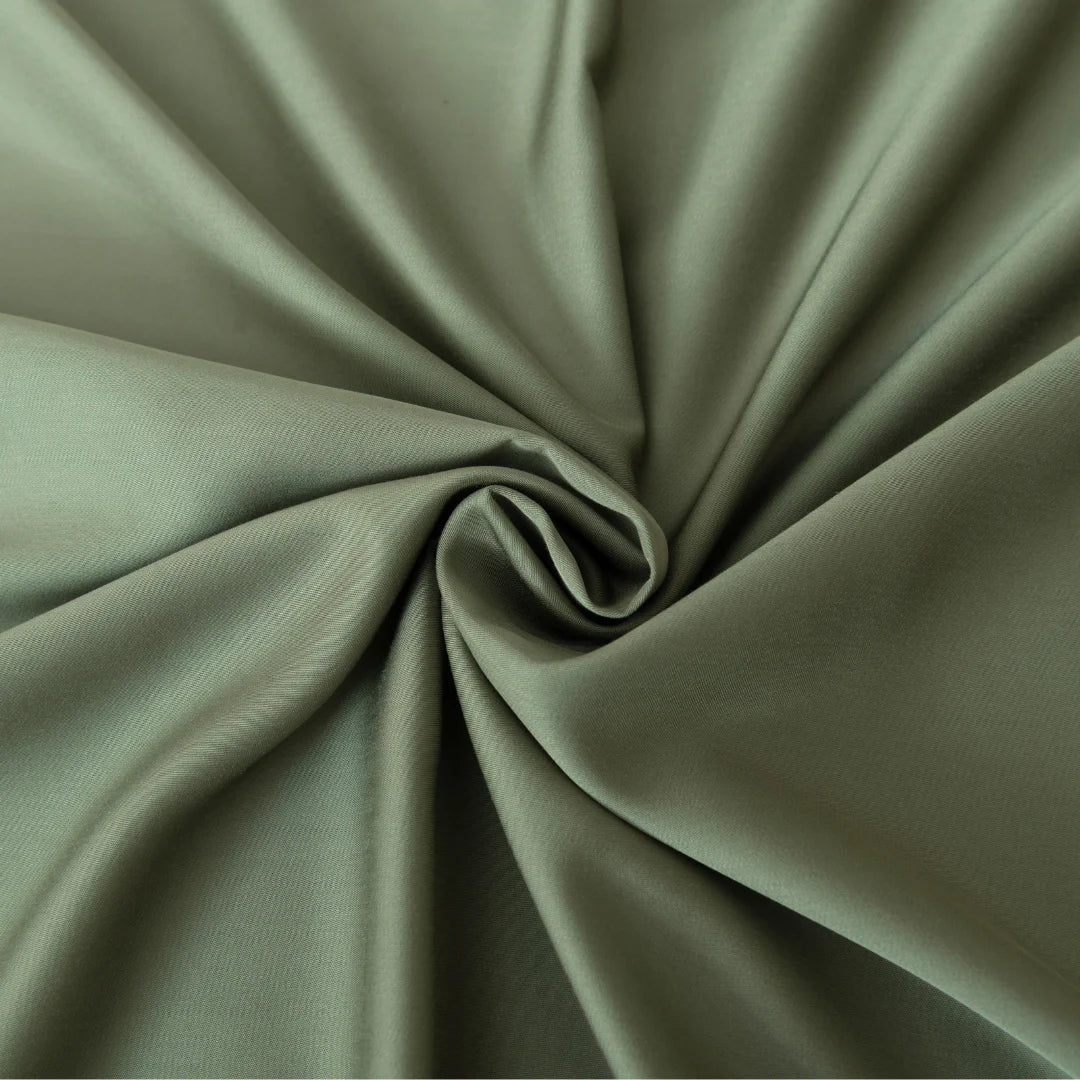 An elegant swirl pattern created from a luxurious sage green fabric with a satin weave, highlighting the graceful folds and soft shadows is captured in the Linenly Bamboo Pillowcase Set in Moss.