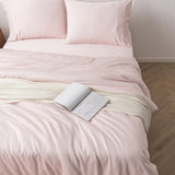 A serene and inviting bedroom scene offering a luxurious sleep experience with a neatly made bed covered in soft pink Rayon from Bamboo sheets and a cozy Linenly Blush Bamboo Quilt Cover draped across, with an open