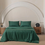 In a bedroom decorated with a Linenly Bamboo Quilt Cover Set - Evergreen, a bed adorned with green pillows sits against an arch-designed white wall. A wooden nightstand holds a lamp, candle, and clock. The premium bamboo materials provide silky comfort, while a textured rug completes the room.