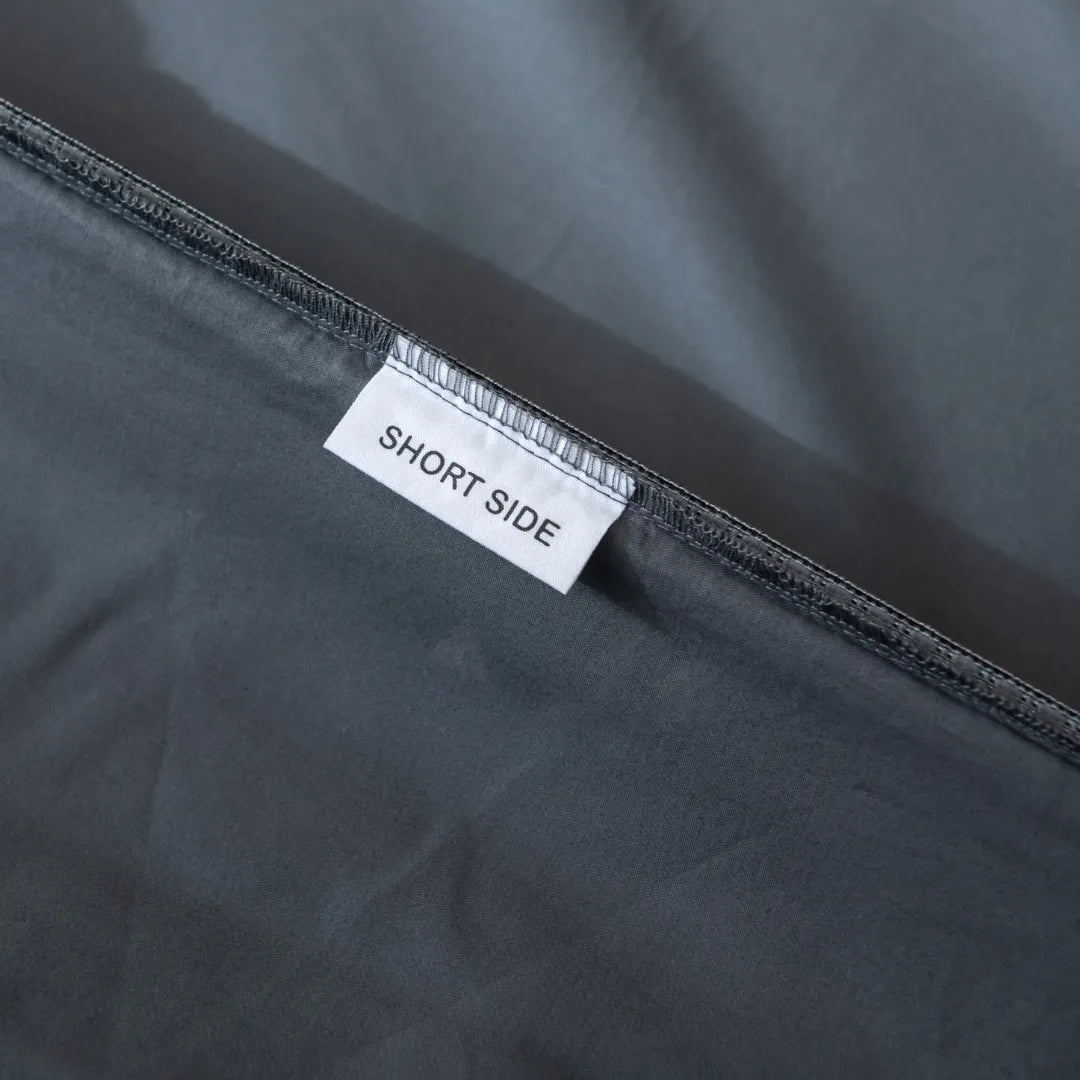 A close-up of a gray seam on the Linenly Luxe Cotton Sateen Fitted Sheet in Charcoal, featuring a white "SHORT SIDE" label—ideal for modern bedding made from long-staple cotton.